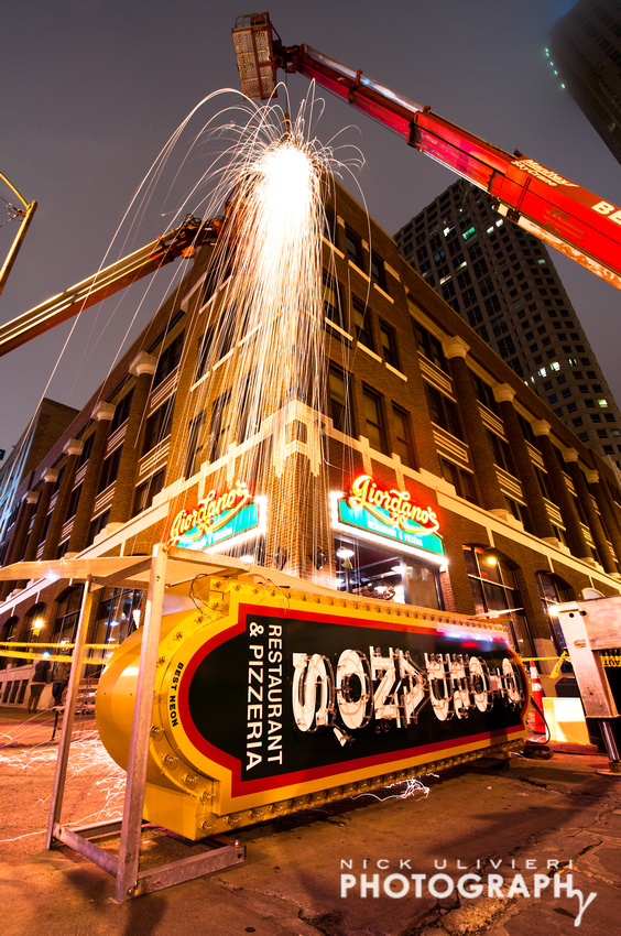 Sparks rain down on the street as workers prep the existing structural support to accept the new sign