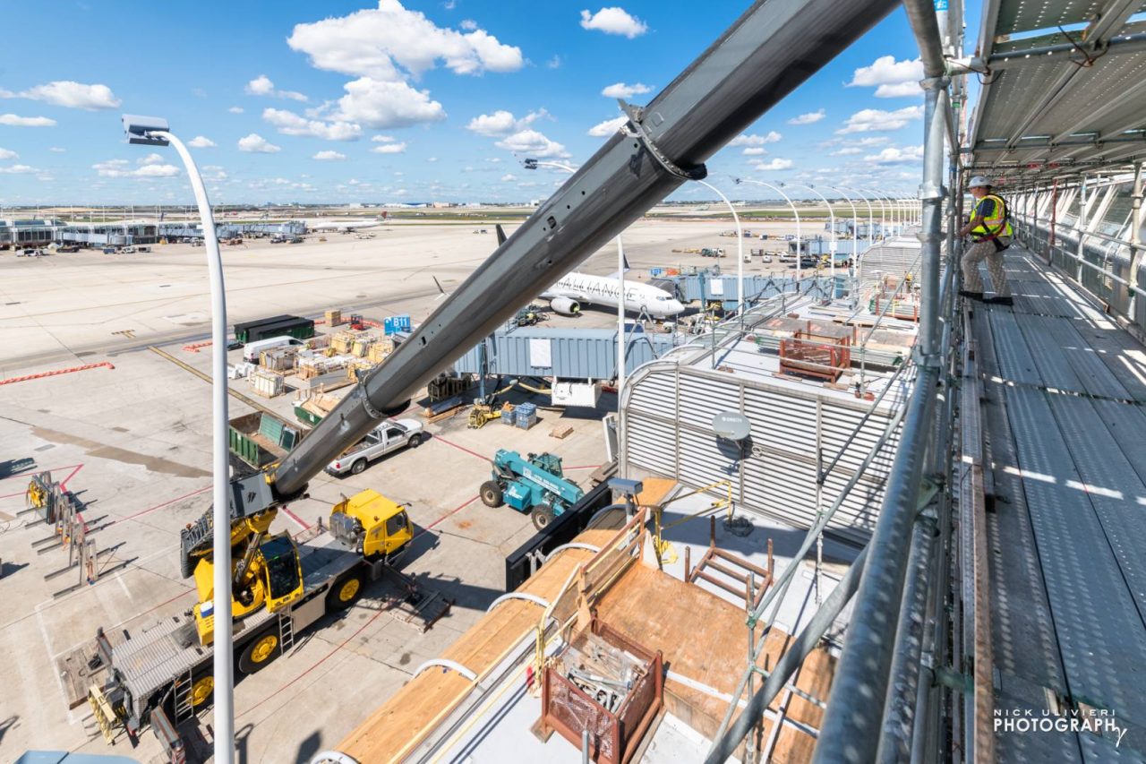 A large crane lifts material into pace. One gate over, an airplane awaits passengers 