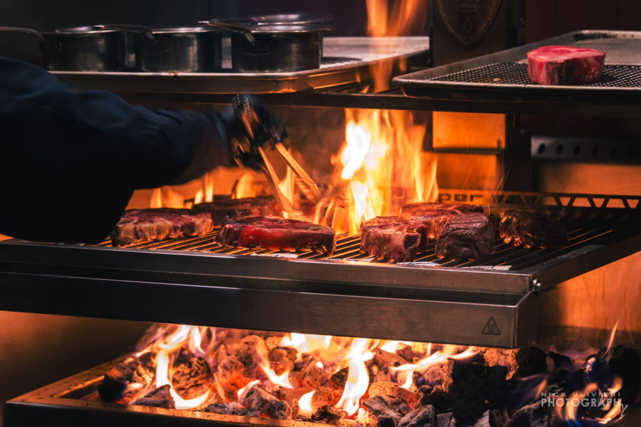 A roaring hot fire flares up as stears are seared in view of restaurant guests