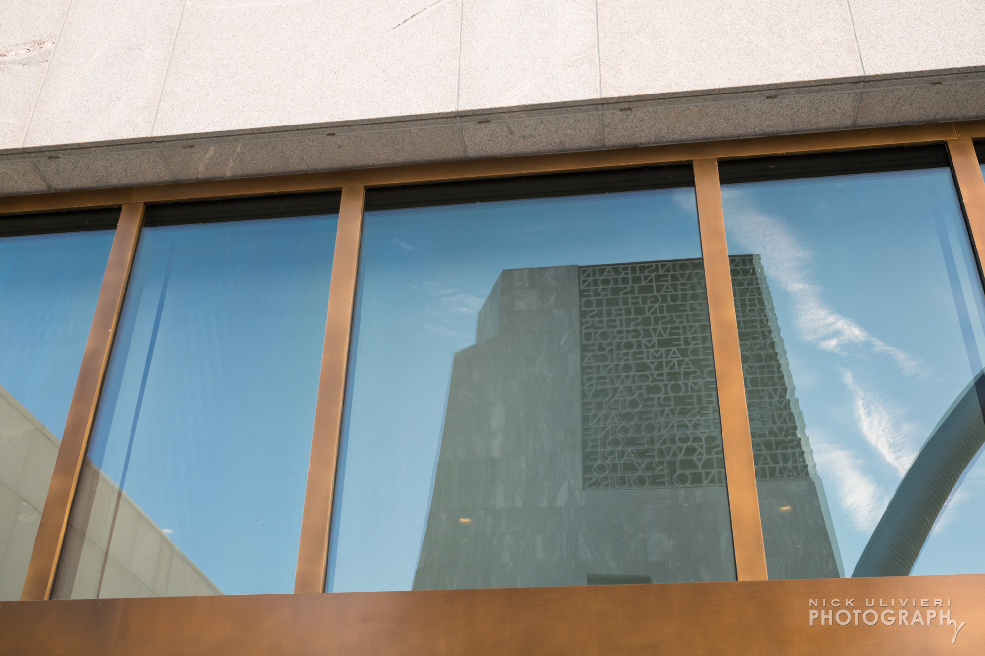 The Museum tower is reflected in the glass windows of the low-slung Public Library building. Bronze-colored window mullion are featured thought the campus architecture.