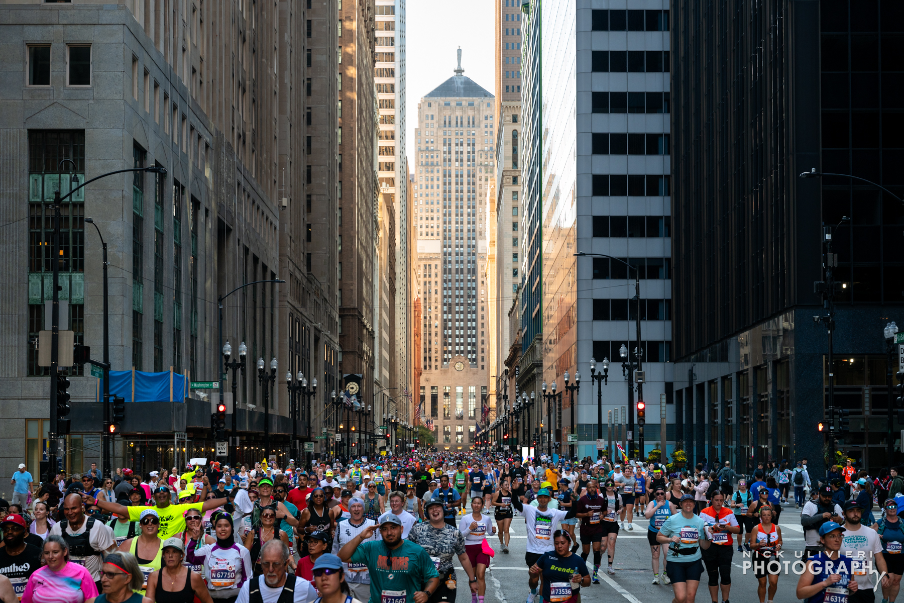 A cityscape photo of LaSalle St canyon in Chicago and the Chicago Board of trade building capping off the street with thousands of Marathon runners in the foreground